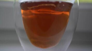 In cup with fragrant tea standing on windowsill, pour few spoons of sugar and mix drink to form vortex in glass mug. Sunlight is around. Morning beverage for breakfast. video