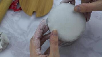 Women's hands put piece of clay on bottom of gray flowerpot. Clay for modeling. Preparation of material for manufacture of ceramic products. Handmade and craft. Wooden tools on marble table. video