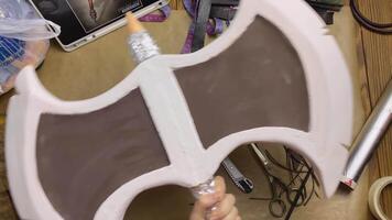 Celtic axe made of penoplex and eva foam with foil on handle in women's hands. Hatchet for festival or performance on wooden table. Cosplayer workshop. Handicrafts and diy. video