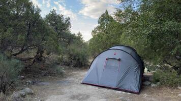 Large gray camping tent surrounded by green trees under a clear sky. The composition includes open space for text, making it suitable for design or promotional use. photo