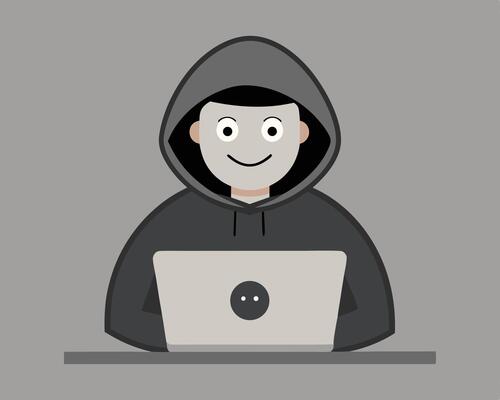 Anonymous hacker wearing a hoodie working on laptop computer on a gray background