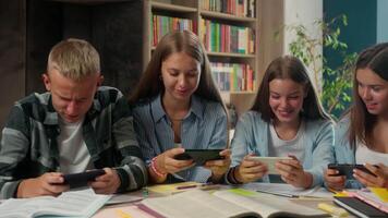 Caucasian four classmates school pupils students friends playing mobile phones smartphones virtual game in class addicted teens in class lesson together internet addiction dependency education problem video
