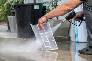 Technician using high pressure water gun for cleaning air conditioner filters. photo