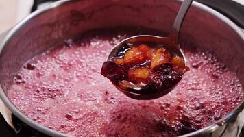 Peach and black plum jams are showing in a spoon in slow motion video