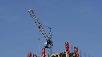 A large crane operates on a construction site, assisting in lifting materials for a high-rise building surrounded by scaffolding and clear skies video