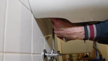 plumber specialist hanging new white ceramic sink on tiled wall in bathroom and tightening nuts with wrench by touch, plumbing work concept, video