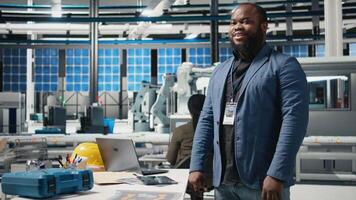 Black master engineer in suit verifies solar panel production in factory, representing technical precision and corporate strategy in the future of green energy. Assembly line. Camera B. video