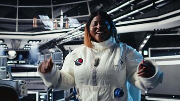 Jolly astronaut waves hand during videocall with Earth command center, documenting results from space experiments. Cosmonaut salutes ground center team, sharing research observations, camera A video