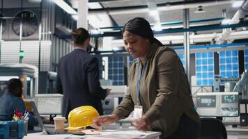 African american female expert reviewing solar panels production line, doing quality control in a photovoltaics factory. Analyzing data reports and insight to create solar power. Camera B. video