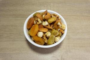 Assorted nuts and dried fruits in a white bowl on wooden surface photo