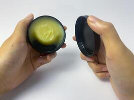 Hands holding a container of hair wax and its lid for grooming and styling photo
