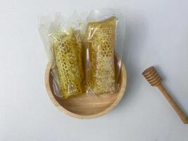 Golden honeycomb in transparent packaging placed on a wooden plate with honey dipper photo