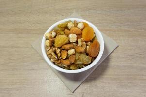 Delicious and Healthy Mix of Dried Fruits and Nuts in a White Bowl on a Wooden Surface photo
