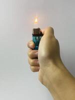 Close-up of a hand holding a lit lighter against a neutral background photo