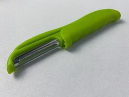 Close-up shot of a green vegetable peeler on a white surface ready for kitchen use photo