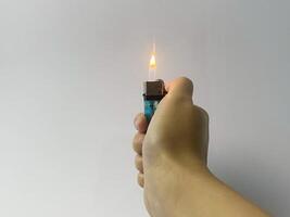 Hand holding a lit lighter against a plain white background in a studio setting photo