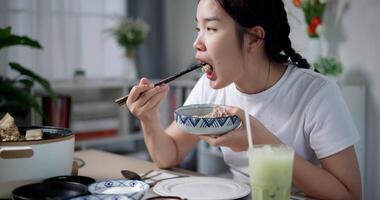 Handheld shot, Young Asian woman is sit at a dining table, enjoying a bowl of noodles with chopsticks video