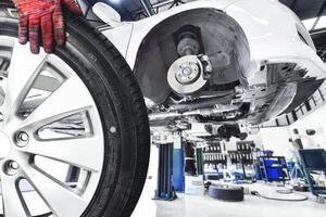 Wheel Alloy Tire Change in Auto Repair Garage, A mechanic hand holds a car wheel, removed from a white car elevated on a lift in a auto service garage. photo
