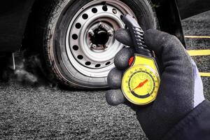 Tire Pressure Check, Auto mechanic wearing a glove checks a car tire air pressure with a yellow gauge, with the wheel and flat tire in background. photo