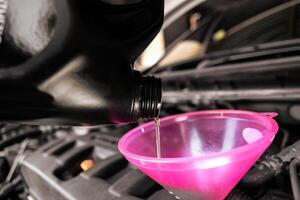Engine oil or motor oil, is being poured from a dark bottle into a pink funnel in a car engine bay. photo