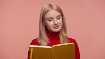 Woman reading yellow notebook and nodding in approval on pink background video