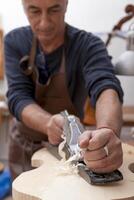 skilled violin maker in the workshop planing a piece of wood to make a violin - focus on hand photo
