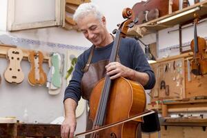 mature luthier playing a viola using the bow to test the sound quality at work photo