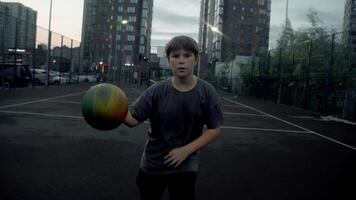 At dusk, a teenage basketball player tries to outdo another player by using dribbling skills, aggressively playing on a basketball court in a residential area of the city. POV video