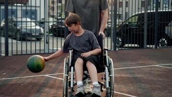 Father and his son with special needs enjoy spending time together in evenings, playing basketball on nearby playground. They actively engage in sports and have fun while sun sets behind them. video