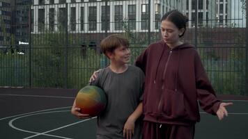 Mother and son have just finished playing basketball together, and they are walking off court. mother is supporting her son, and they both have big smile on their faces. video