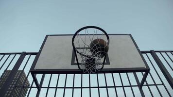 A basketball, after a series of bounces, finally hits the hoop in the evening on the outdoor sports court in the city. Slow motion. below video