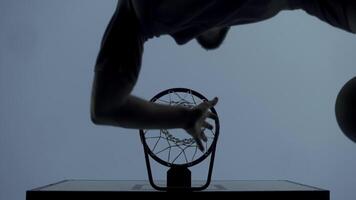 A young man throws a basketball directly from under a basketball basket in the evening outdoors. jump shot. below video