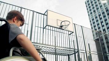 Young boy with unique health requirements and wheelchair is attempting to propel ball into basketball hoop, but he is unsuccessful, and this causes him to become frustrated. video