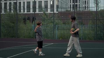 Two brothers finished their basketball game in the evening on the court. They shook hands and hugged, having a friendly conversation, before heading home. video