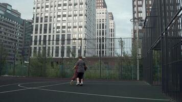 Young mother and her teenage son are playing basketball on the court. They are having a great time and enjoying the experience together. video