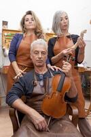 portrait of three middle-aged violin makers posing showing new violins in their workshop photo