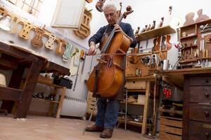 mature violin maker craftsman playing a newly made viola using the bow to hear the sound at the workplace photo