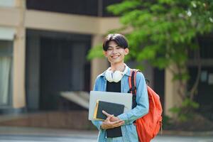 A cheerful Asian college student stands outside on campus with a backpack, smiling and looking at the camera. photo