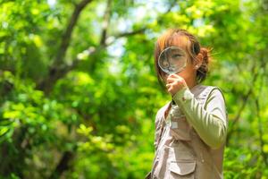 Happy little girl is exploring in the forest and looking for insects with a magnifying glass. Adventure tourism and learning concept. photo