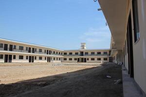 School building with two stories, having cream-colored walls and a flat roof, arranged in a U-shape with an open courtyard in the center. photo