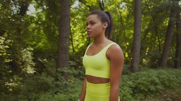 A young African American woman runs through a vibrant park, surrounded by lush greenery. She is dressed in bright athletic wear, embodying a commitment to fitness and wellness. video