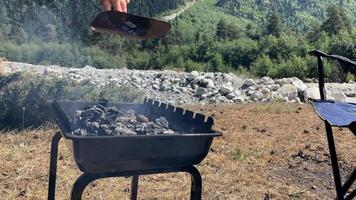 A person barbecues outdoors in a scenic mountain setting, emphasizing leisure, nature, and summer activities visible are Caucasian hands and grilling tools video