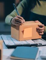 A woman is writing on a piece of paper with a pen and a box with a sticker on photo