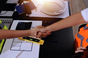 Two people shaking hands at a desk with construction tools photo