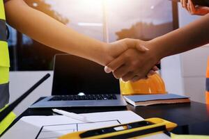 Two people shaking hands over a table with a laptop photo