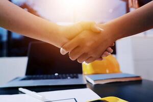 Two people shaking hands over a desk with a laptop photo