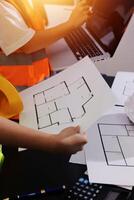 A man in an orange vest and safety vest is holding a laptop and paper with blueprints photo