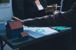 A man and woman are sitting at a table with a house and recycling symbol photo