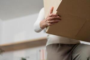 Moving and Lifting. Close-up of woman lifting a cardboard box during relocation. photo