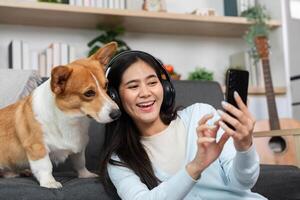 Pet-Friendly Remote Work. Young woman laughing with her dog while using a smartphone at home. photo